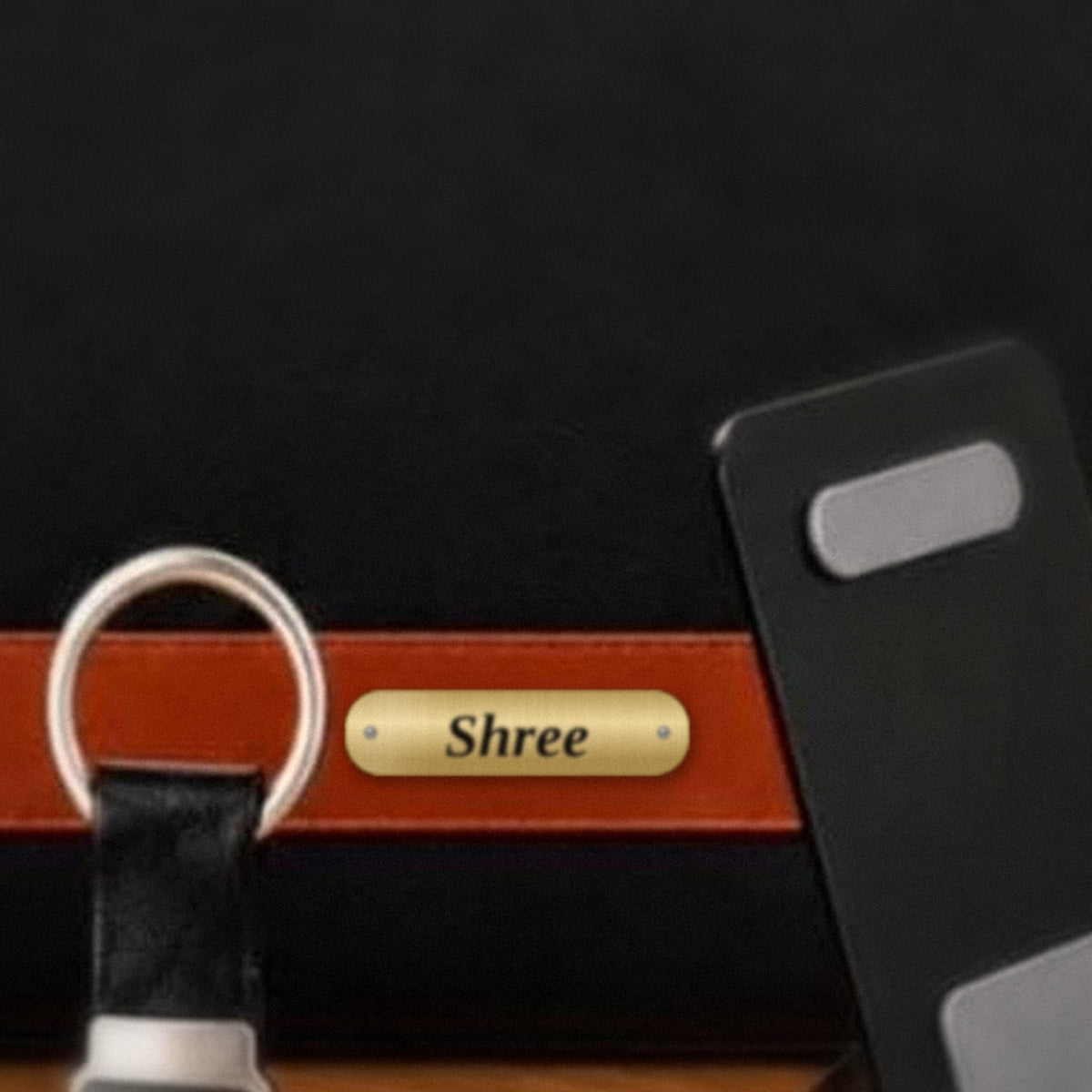 Brass nameplate with a black engraved name on the tan strap of a laptop bag